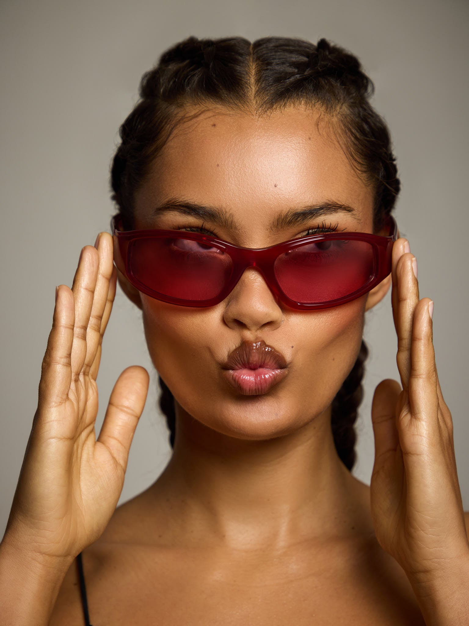 Woman wearing ace red oval sunglasses and making a playful face against a neutral background