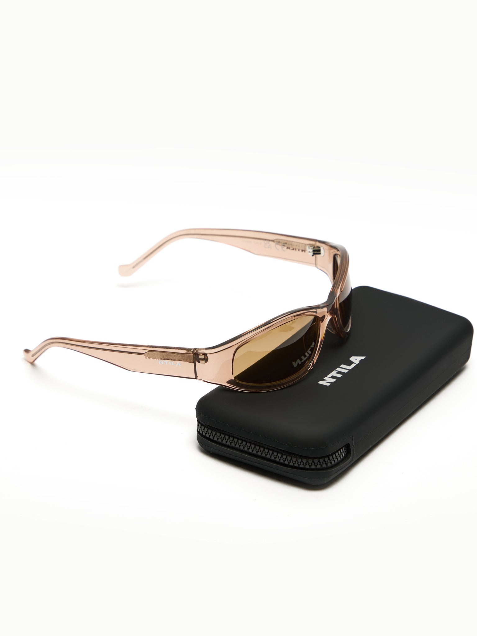 Brown rose gold NTILA Ace oval sunglasses on a black carrying case with 'NTILA' branding on a white background
