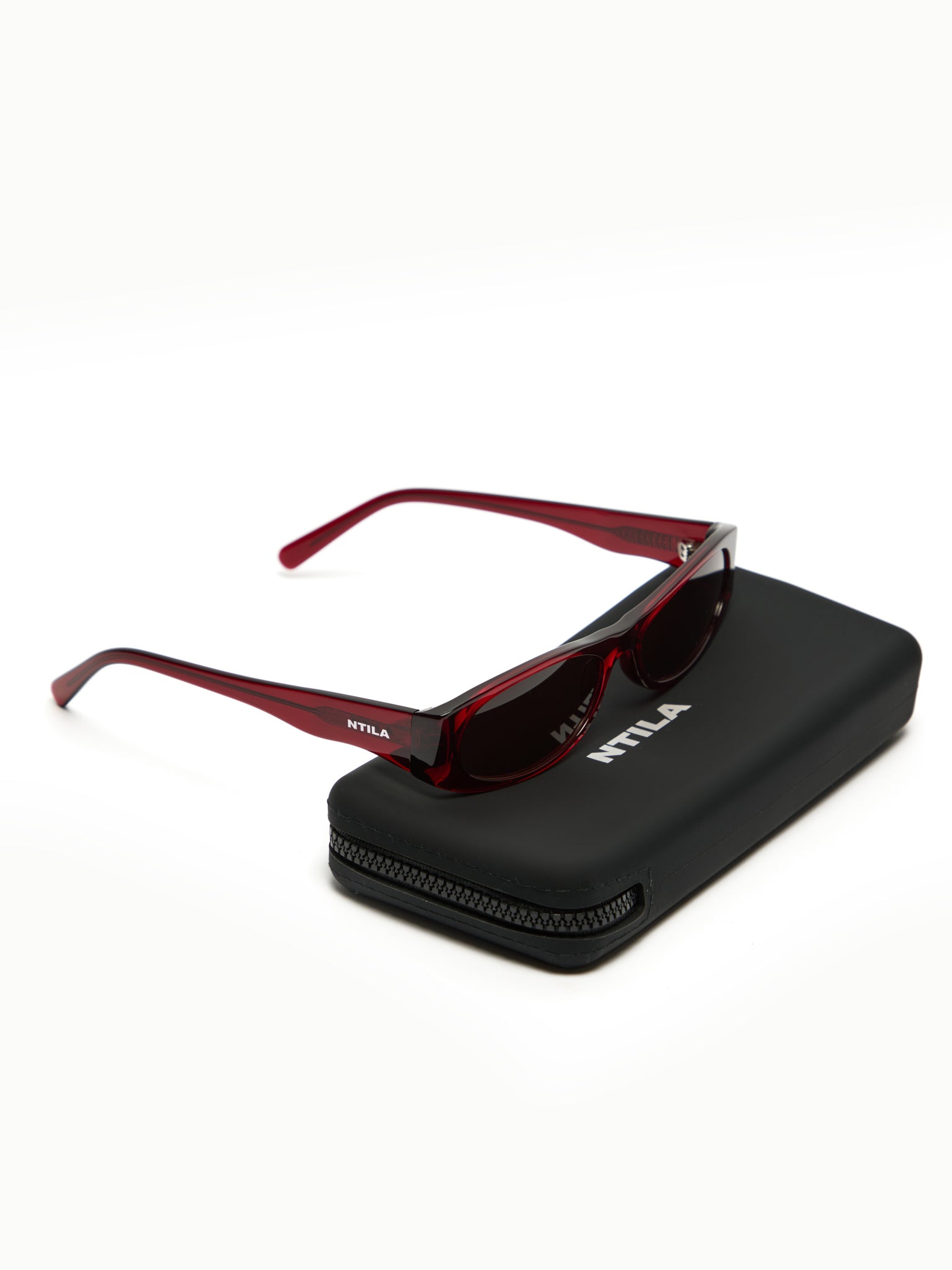 Red wine NTILA Leni sunglasses with a black case on a white background, featuring the NTILA brand.