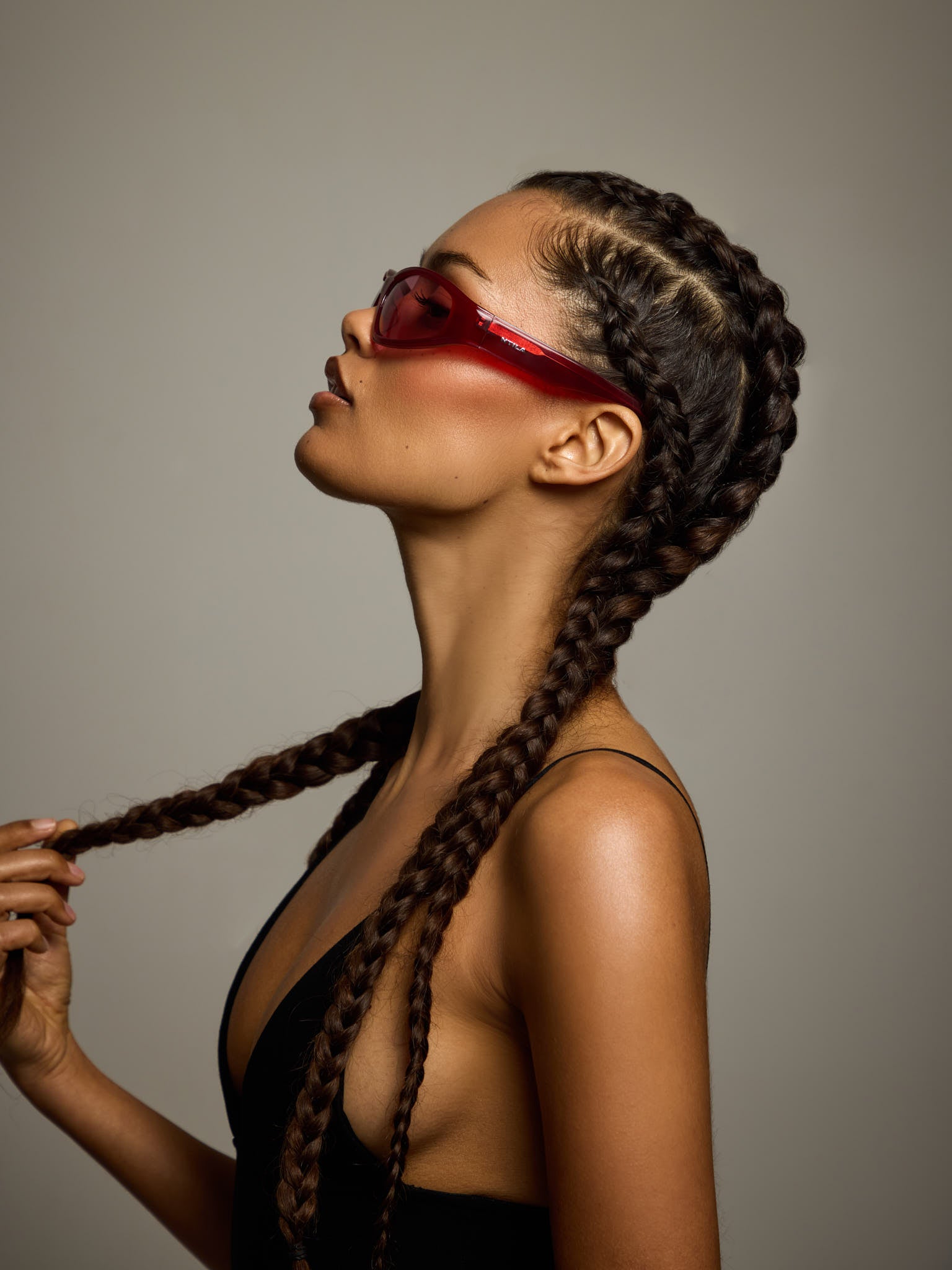 Woman with braided hair wearing ace red oval sunglasses against a neutral background