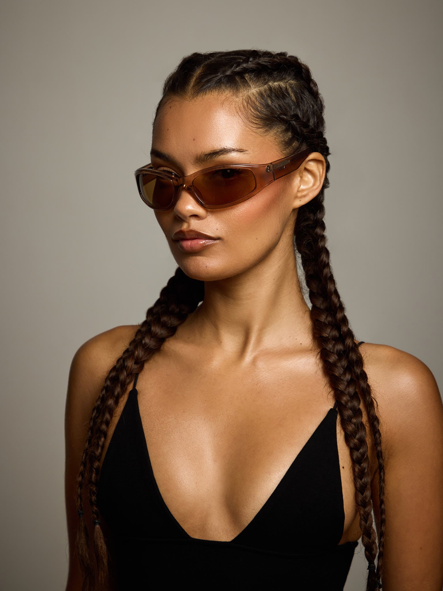 Woman with braided hair wearing ntila Ace brown toffee rose gold oval sunglasses against a neutral background