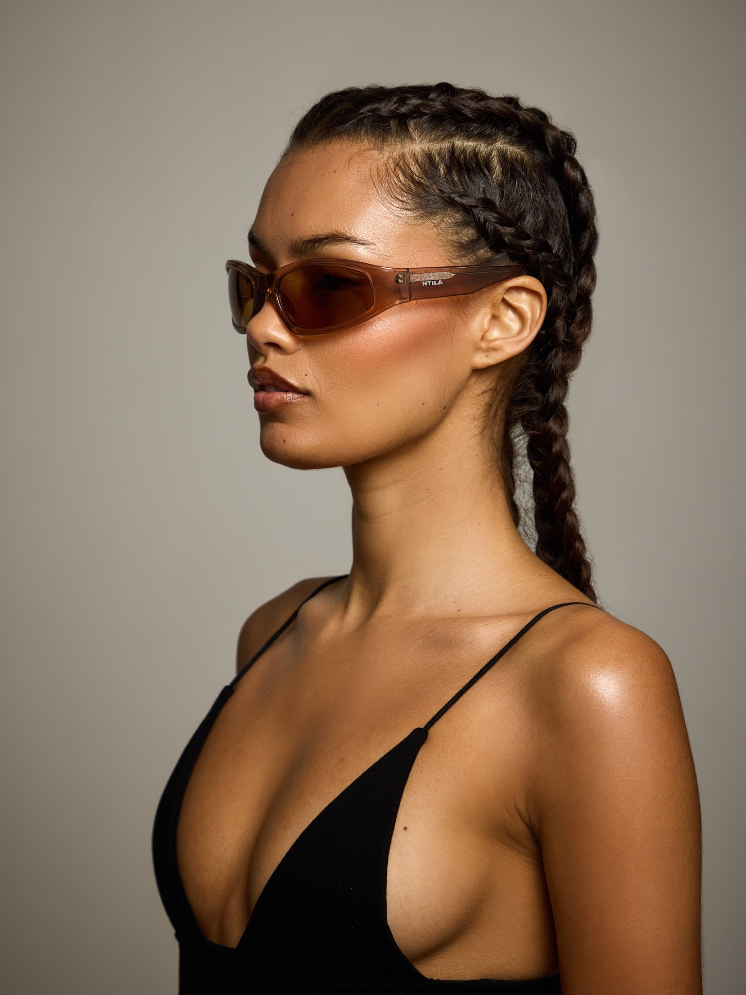 Woman wearing NTILA Ace toffee brown oval sunglasses against a neutral background