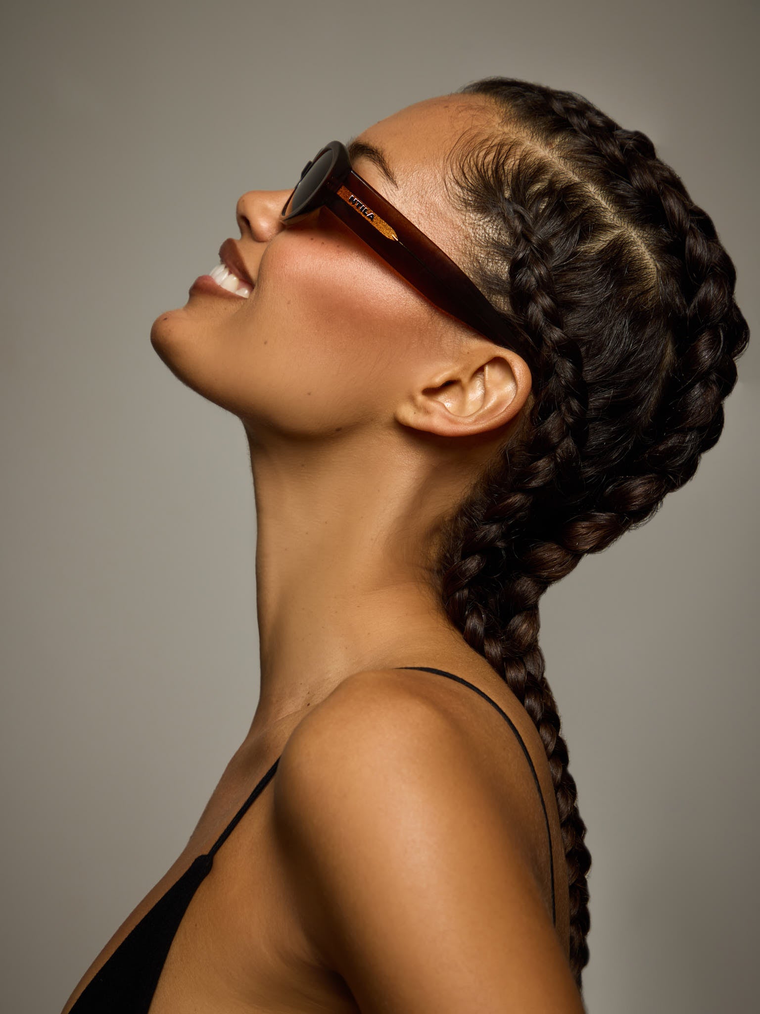 Woman with braided hair wearing Cleo brown oval sunglasses against a neutral background
