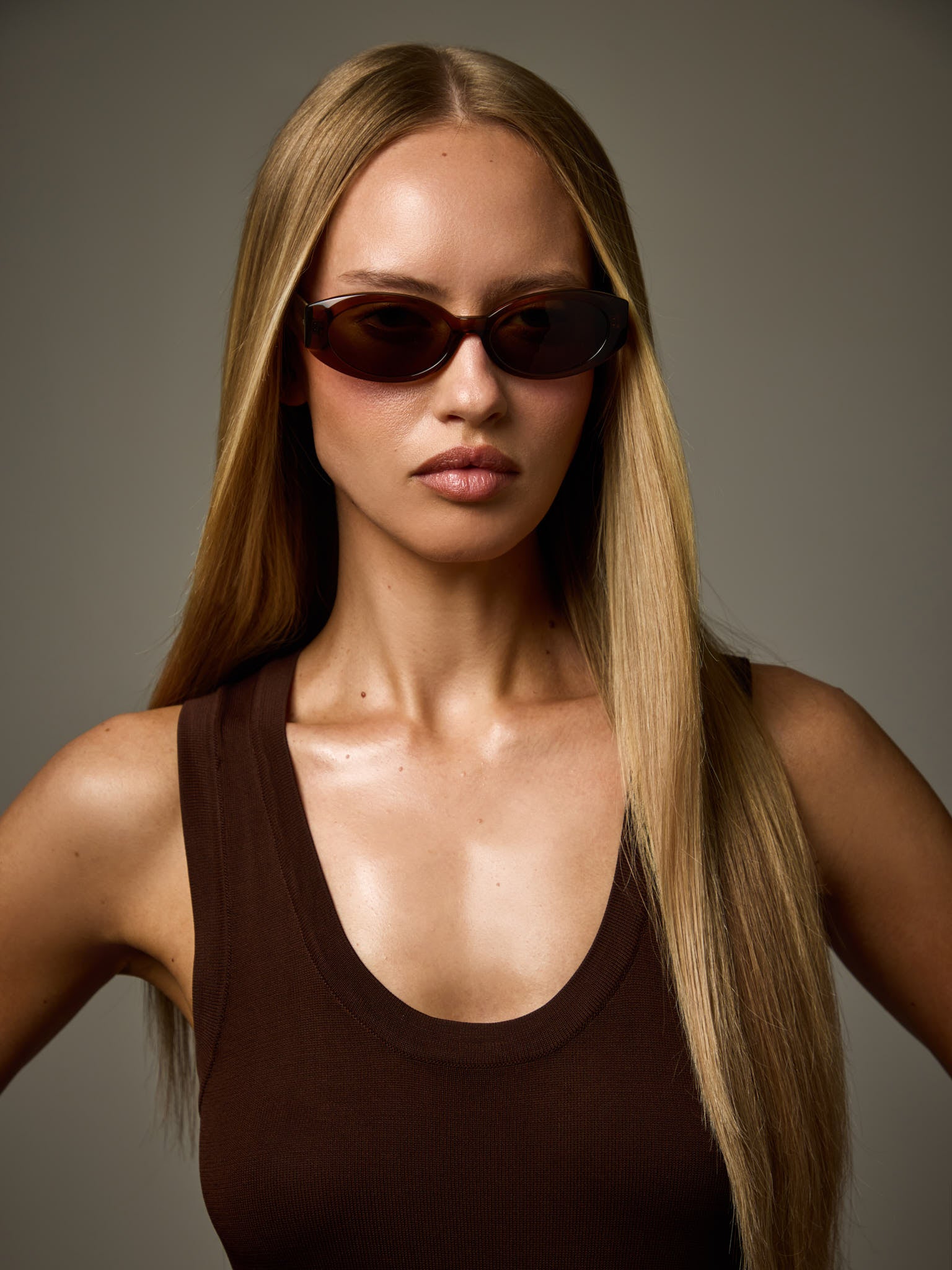 Woman wearing Cleo brown oval sunglasses against a grey background