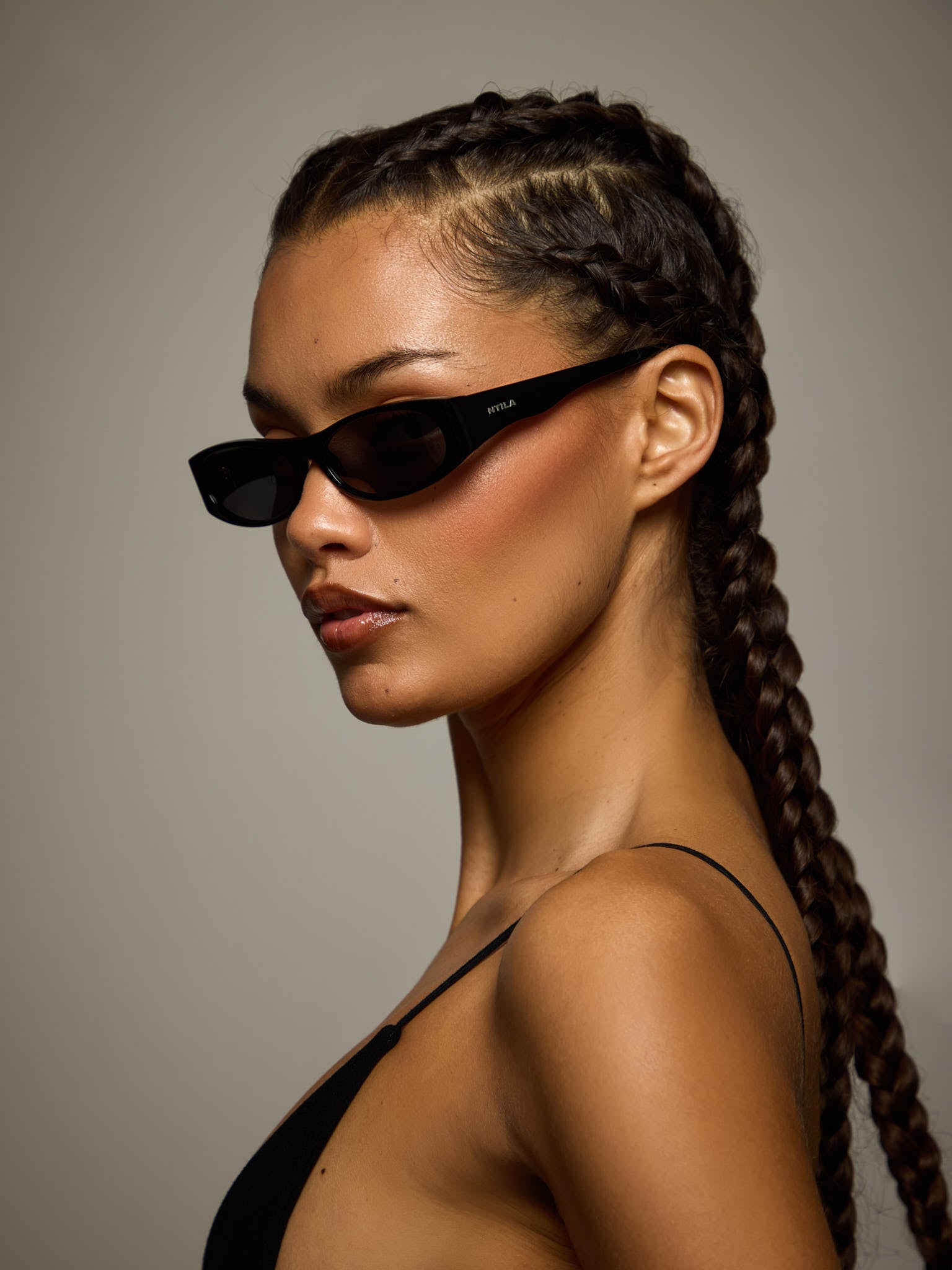 Woman with braided hair wearing NTIL black Leni sunglasses against a neutral background