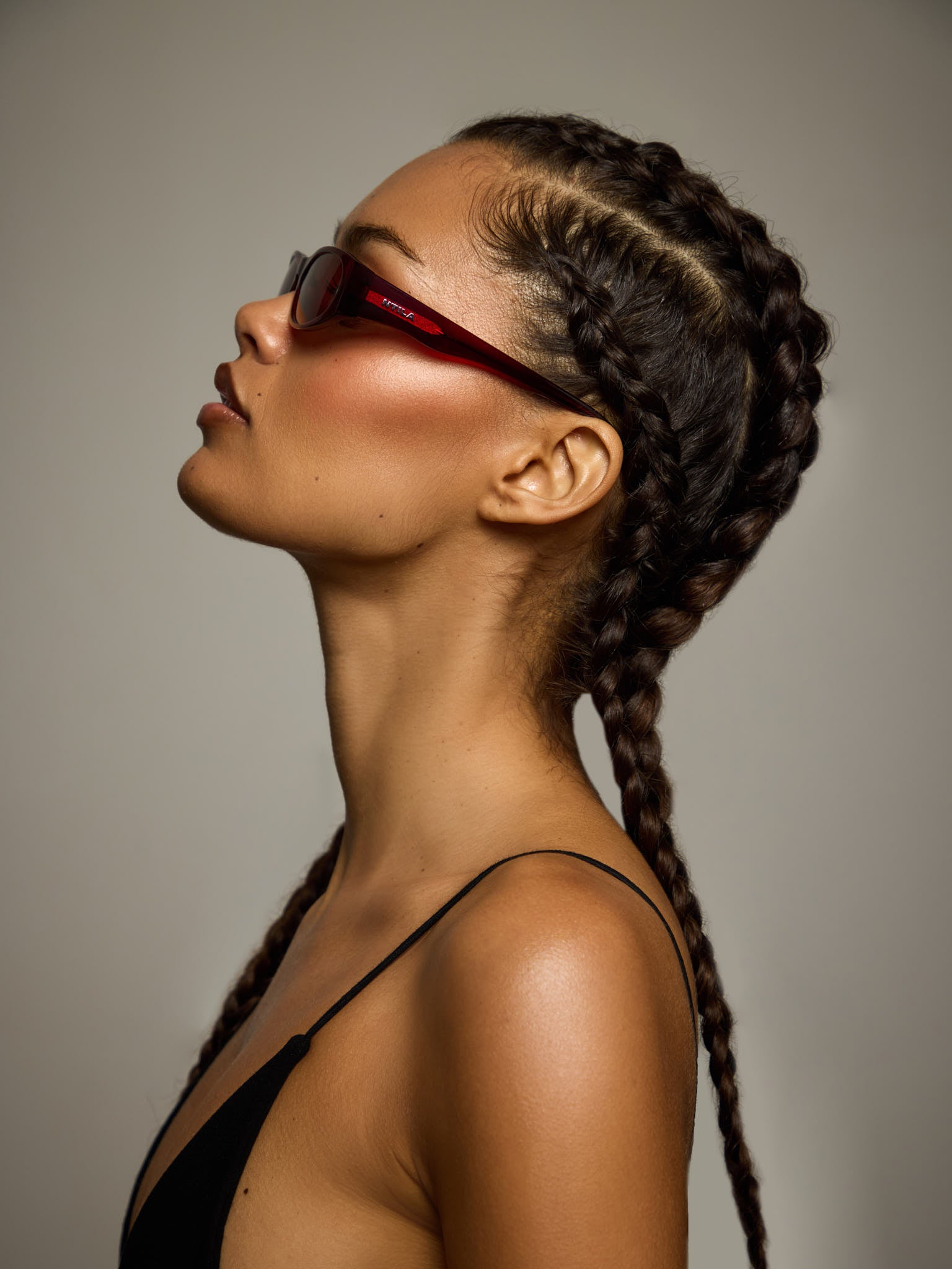 Woman with styled braids wearing NTILA red wine Leni sunglasses against a neutral background