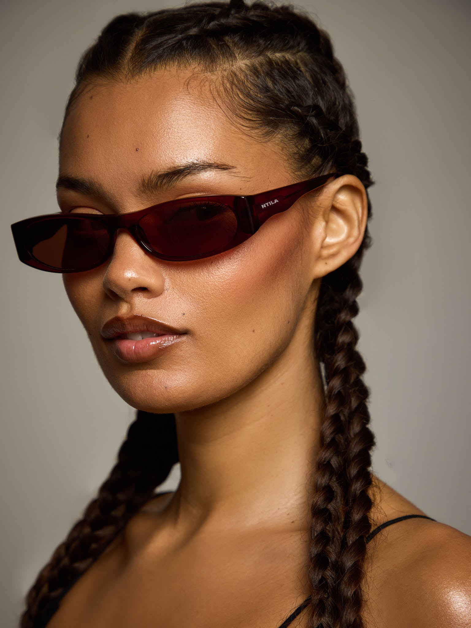 Woman wearing NTILA red wine Leni sunglasses with braided hair against a neutral background