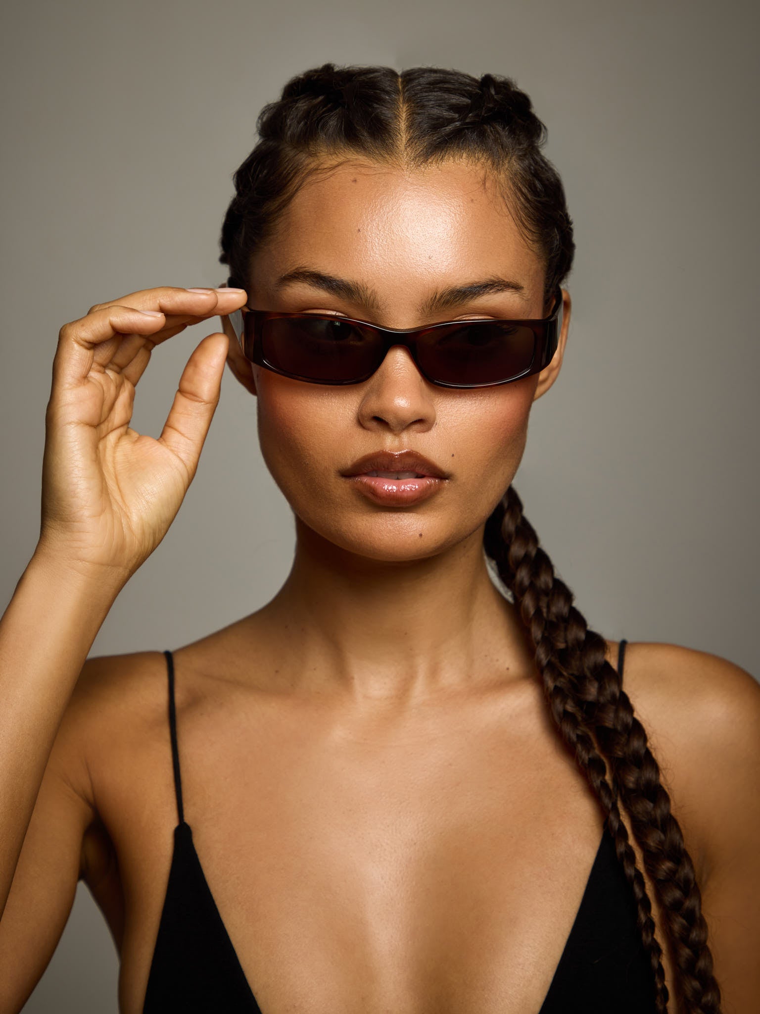 Woman wearing ntila black tort tortoise shell roko sunglasses with braided hair against a neutral background
