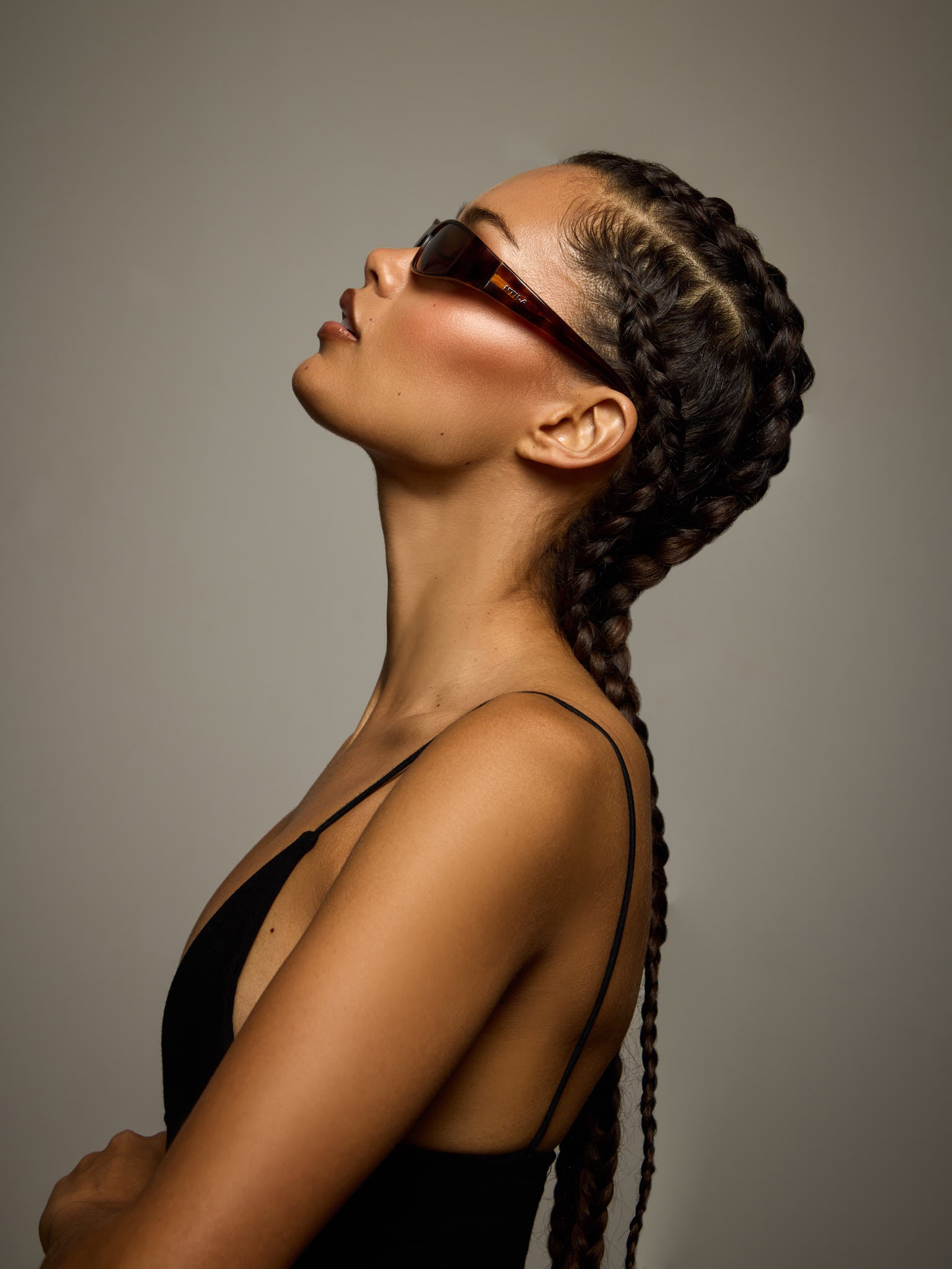 Woman with braided hair wearing NTILA black tort tortoise shell Roko sunglasses against a neutral background